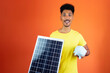 Handsome Black Man Holding a Piggy Bank and Solar Panel Isolated on Orange. Man in a yellow shirt isolated.