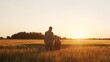 © Acronym - Farmer and his son in front of a sunset agricultural landscape. Man and a boy in a countryside field. Fatherhood, country life, farming and country lifestyle.