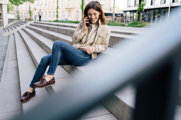 Wall Mural - Young woman sitting on stairs and talking on phone