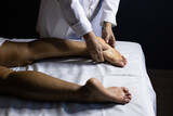 Fototapeta  - Detalhe das mãos de massagista aplicando massagem terapêutica no pé de um paciente que está deitado em uma maca com lençol branco.