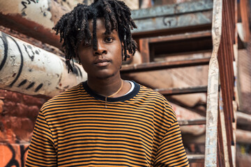 Young handsome stylish black man with natural hair dreadlocks. Afroamerican guy.Stairs,wall painted with graffiti in poor quarter of street art culture city district.African american skateboarder man