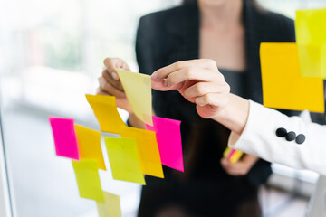 Close up hands of Asian businesswomen. Brainstorm meeting with colorful sticky paper notes on the glass wall for new ideas. Using agile methodology for business in a tech start-up office.