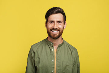 Portrait of happy middle aged man posing and smiling at camera over yellow studio background, copy space