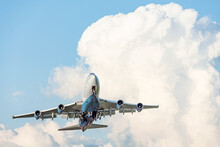Large four-engine aircraft gracefully takes off by retracting the landing gear against the backdrop of beautiful white cumulus clouds.