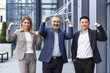 © Liubomir - Successful diverse business team, man and woman outside office building smiling and looking at camera, portrait of business people in business clothes, colleagues holding hands up and rejoicing