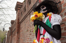Low Angle View Of A Woman In A Costume Of Calavera Catrina Holding Flowers With Both Hands Outdoors
