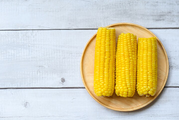 Wall Mural - cooked sweet corn on wooden plate background, ripe corn cobs steamed or boiled sweetcorn for food vegan dinner or snack