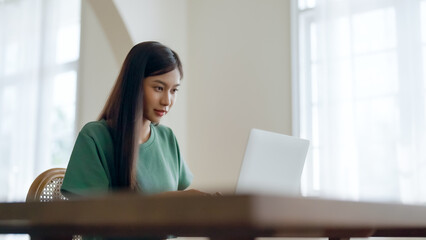 Wall Mural - Young asian woman working at home. Female using computer laptop on desk at house