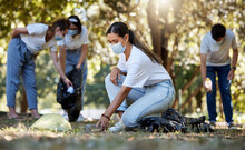 Group Of Volunteers Picking Up, Cleaning And Reducing Pollution In A Public Nature Park Together. Diverse Community Wearing Face Masks To Protect From Disease, Collecting Dirt And Doing Cleanup
