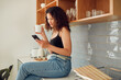 © Kay Abrahams/peopleimages.com - Woman texting, chatting on the phone while relaxed, carefree and sitting on kitchen counter. Young, relaxing and casual female student at home looking at social media, pictures or videos
