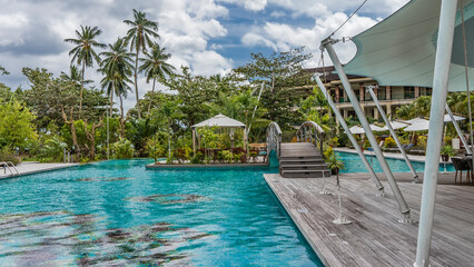  Recreation area in the hotel: swimming pool, arch bridge, gazebo. Lush tropical vegetation all around. Clouds in the blue sky. Seychelles