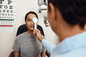 Canvas Print - Eye exam, vision testing at an optometrist with young woman and doctor. Opthamologist using an occluder to test eyesight before being fitted with glasses. Relaxed lady smiling, satisfied with service