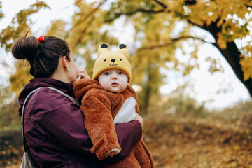  A woman walks in the park in autumn with her child. A young woman holds her baby in her arms and stands under a tree.