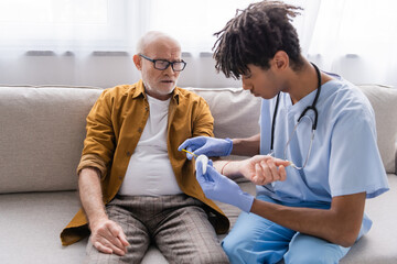 African american nurse doing injection to senior man on couch at home.