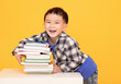  Happy little boy holding large books isolated on yellow background