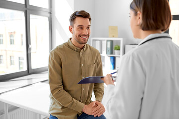 Canvas Print - medicine, healthcare and people concept - female doctor showing clipboard to smiling man patient at hospital