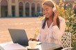 © Paulista - Happy young woman attending a web conference via headphones or freelancer working at laptop, sitting in a outdoor cafe table.