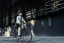 Businessman Riding Bicycle In Front Of Modern Office Building.
