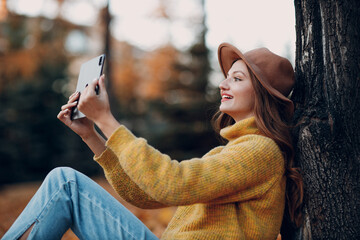 Young woman model sitting with tablet pc in autumn park with yellow foliage maple leaves. Fall season fashion