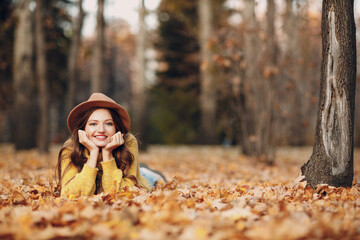 Young woman model lying in autumn park with yellow foliage maple leaves. Fall season fashion