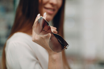 Close up of gorgeous young woman smiling picking and choosing glasses at the optician corner at the shopping mall. Happy beautiful woman buying eyewear eyeglasses at the optometrist.