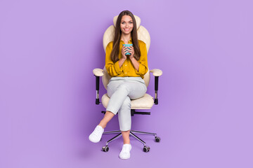 Wall Mural - Full length portrait of positive lady sit chair hands hold coffee cup isolated on purple color background