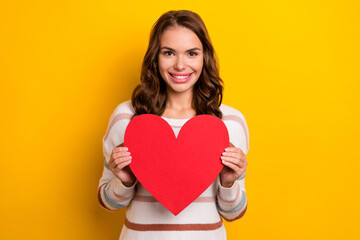 Wall Mural - Portrait of pretty positive girl toothy smile arms hold heart postcard isolated on yellow color background