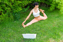 Woman Doing Front Splits With Bind Near Laptop In Park