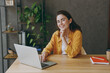 © ViDi Studio - Young smiling fun happy successful employee business woman wear casual yellow shirt hold use laptop pc computer look camera sit work at wooden office desk with pc laptop. Achievement career concept.