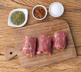 Wall Mural - Rolled beef or roulade, vegetable and bacon stuffed meat over wooden table with seasonings