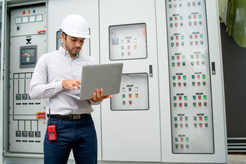 Caucasian engineer man use laptop in front of electrical control panel during process of  maintenance in construction site.