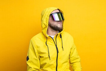 Young man in virtual reality glasses in a yellow jacket looks away on a yellow background