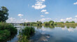Panorama rzeki Odry w tle most lekko pochmurna pogoda, błękit nieba zieleń przy brzegu,  pora letnia, Odra w odcinku województwa Opolskiego
