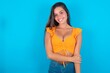 beautiful brunette woman wearing orange tank top over blue background laughing.