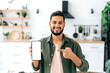 © Kateryna - Phone screen mockup. Smiling indian or arabian young man, showing smart phone with empty white mock-up screen, copy-space for advertising or presentation, standing in living room, looks at camera