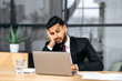 © Kateryna - Fatigue, chronic sleep deprivation. Sleepy arabian or indian business man in a suit, sit at workplace in office with a laptop, put his head on his hand, fell asleep during work, feels tired,overworked