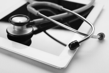 Medical stethoscope and tablet on beige background, closeup