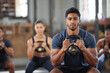 © Alexis Scholtz/peopleimages.com - Personal trainer squatting with a team of athletes in a workout session at a fitness club. Portrait of a fit, active and serious young male coach using a kettlebell and training a group of people