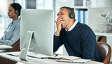 Tired call center agent yawning while sitting at his desk working on a computer in the office. Exhausted, bored and rude man in financial customer service feeling fatigue after a long day at work.