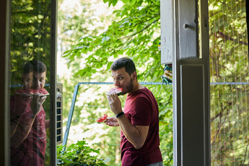 Man eating juicy red watermelon on the balcony. The concept of summer and delicious vegetables. Front view.