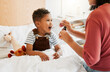© K Abrahams/peopleimages.com - Sick child taking medicine syrup, flu treatment and cold cure for illness, sickness and virus symptoms. Mom caring for health of little son, kid and boy to rest, recover and get better in bed at home