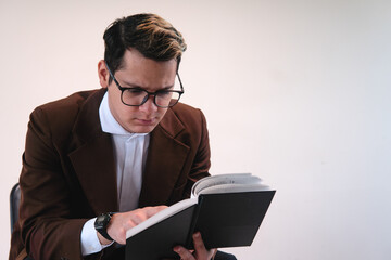 Smartly dressed studious man. Man dressed in brown jacket, white shirt, glasses and on a white background. Business man reading a black book. Lawyer working with his notes. High quality photo