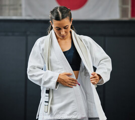 Wall Mural - . Female professional karate student dressing, wearing and preparing for practice, fight or training match in dojo. Woman mix martial art athlete tying uniform before competition or exercise workout.