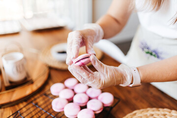 Female hands and two halves of pink macaroons with stuffing close-up. Cookie baking. Macaroons making