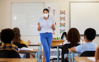 Poster - Young female teaching after covid pandemic, in classroom with young children students, in face mask. Back to school for little kids learning their education from their teacher after quarantine