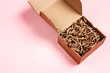 Open brown box with brown shredded paper on pink background. Paper gift box with decorative straws fillers for your product placement. Copy space for produce and text.