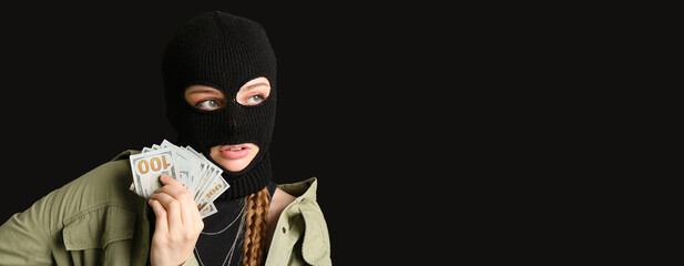 Wall Mural - Young woman in balaclava and with money on black background with space for text