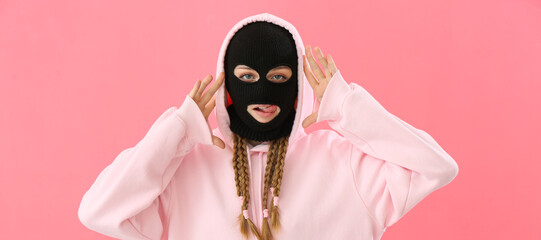 Wall Mural - Young woman in balaclava and hoodie on pink background