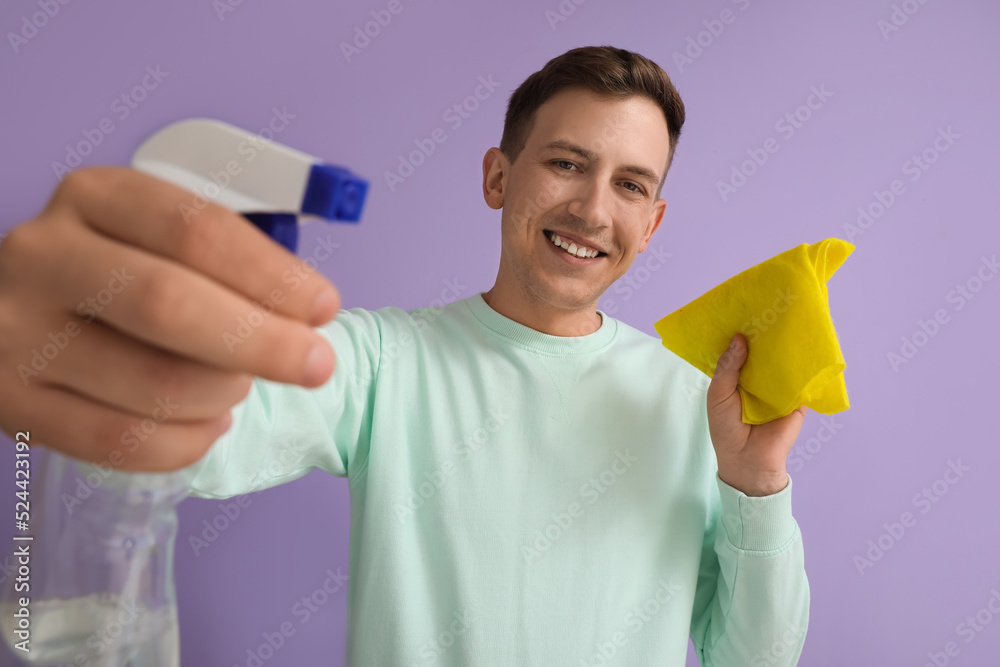 Young man with detergent and rag on violet background