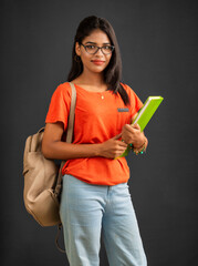 Poster - Beautiful young girl with a backpack standing and holding a notebook, posing on a grey background.